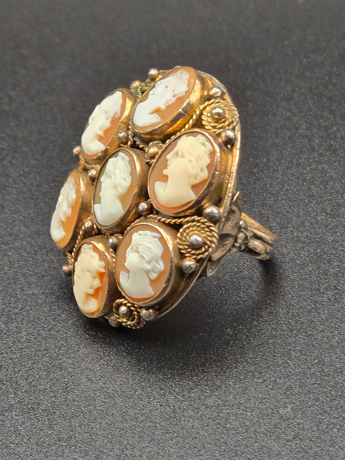 Domed cocktail ring with seven carved shell cameos in a gold-filled filigree setting.